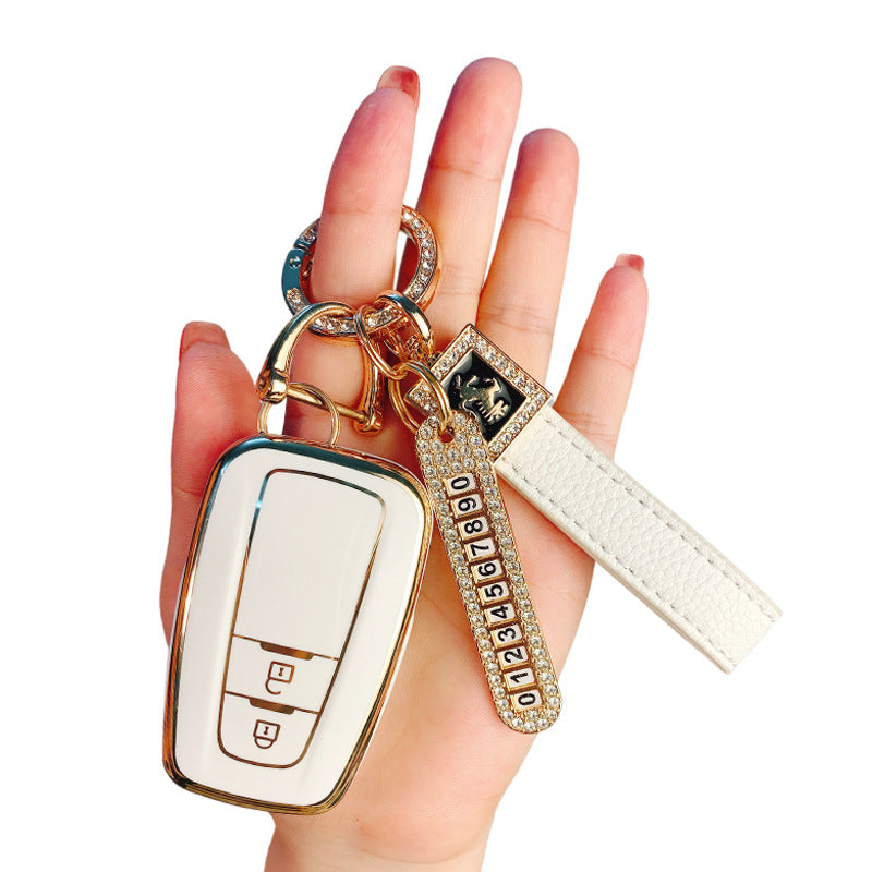 Key fob cover for Toyota 2-button keys – TPU – white and gold cover held in hand with crystal keyring and white leather wrist strap