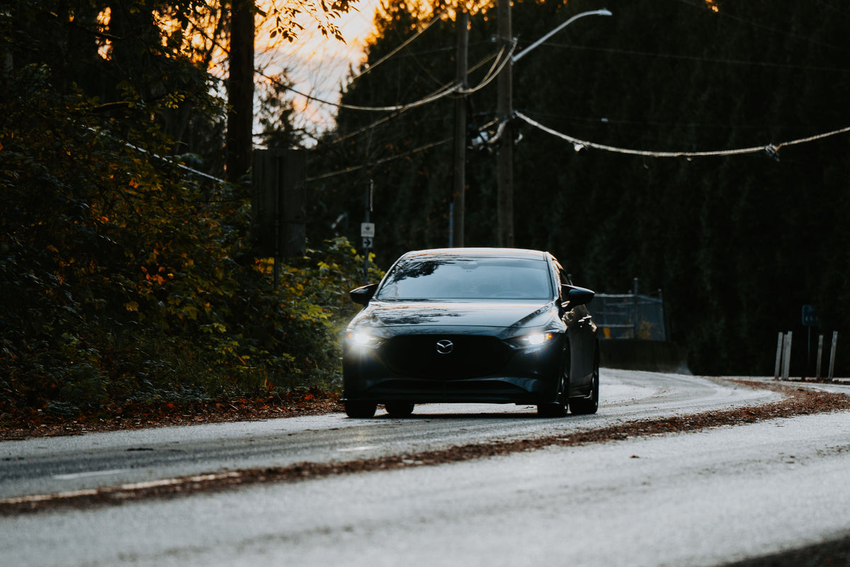 Dark grey modern hatchback with headlights on, on a wet road at dusk