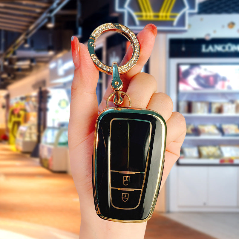 Key fob cover for Toyota 2-button keys – TPU – close-up of black and gold cover held with crystal keyring
